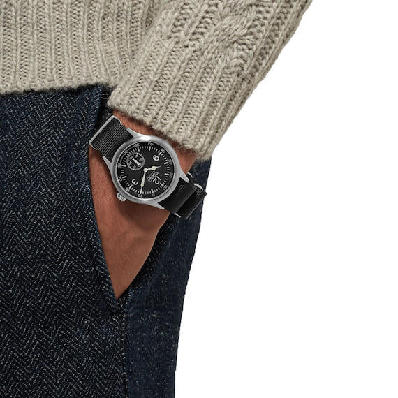Person wearing a Techné Merlin wristwatch with a detailed face, dressed in a beige sweater and dark jeans.