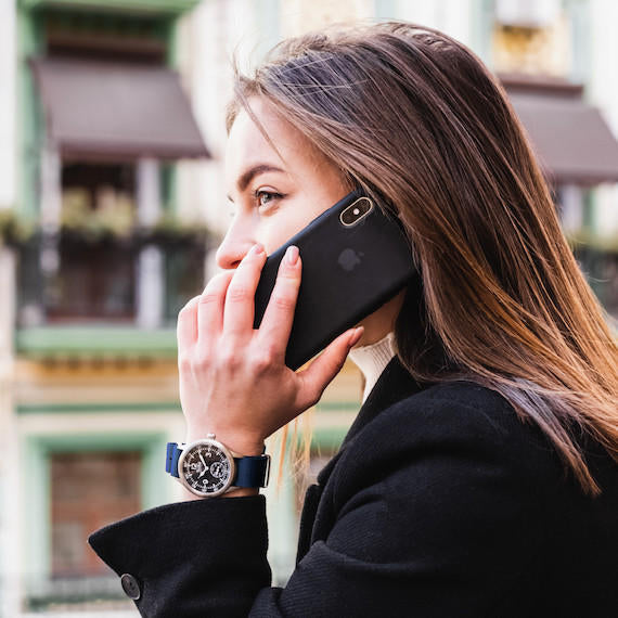 Woman wearing a Techné Merlin watch, talking on a black phone with a blurred background